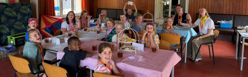Lachende kinderen en leiding genieten samen van een feestelijke maaltijd.