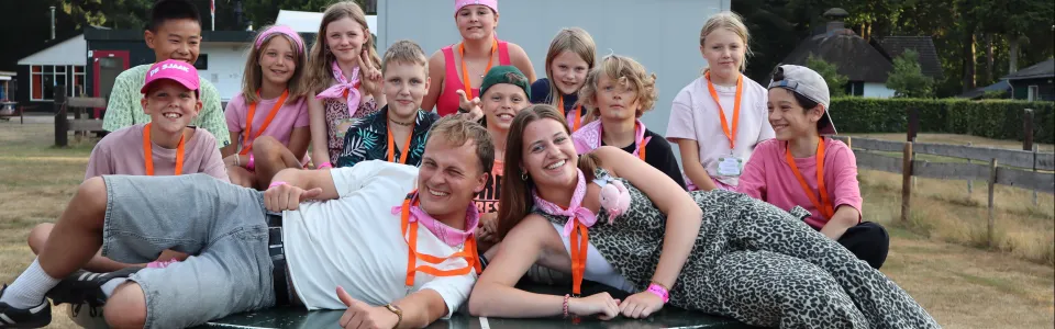 Kinderen en leiding lachen samen rond een tafeltennistafel op kamp