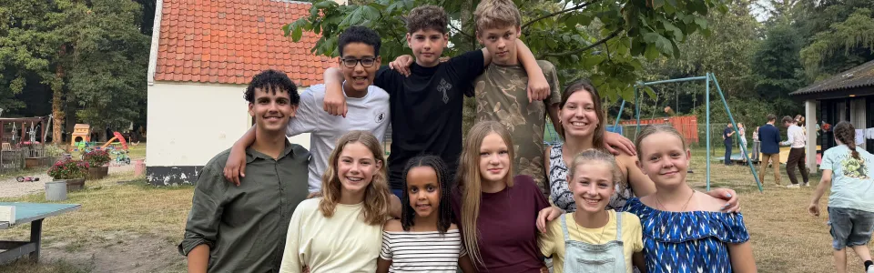 Tieners en leiding poseren lachend samen op het kampterrein