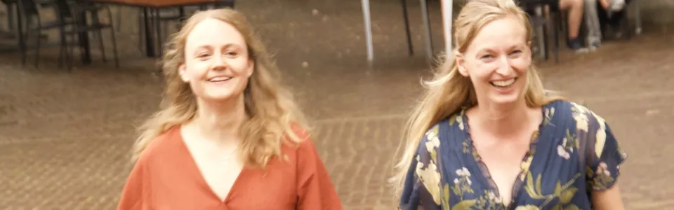 Twee lachende vrouwen lopen samen over het zonnige kampterrein