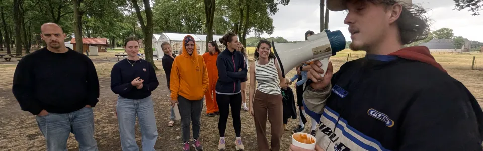Kampleider spreekt vrijwilligers toe met megafoon op het kampterrein