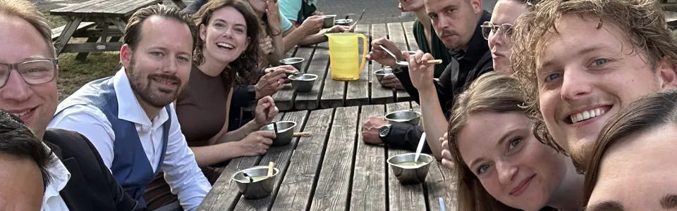 Kampleiding geniet samen van soep aan een lange picknicktafel