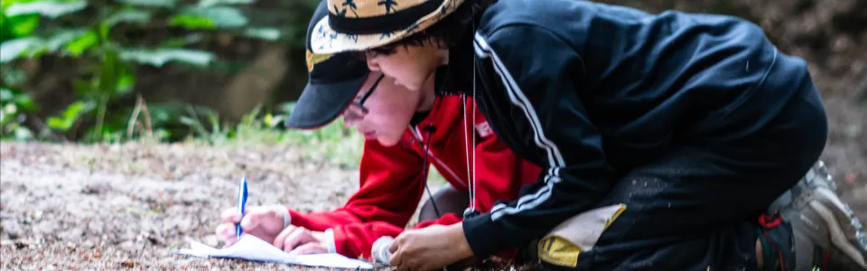 Twee kinderen schrijven samen tijdens een bosspel op brugkamp1