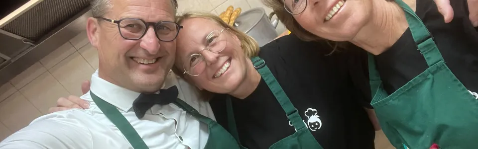 Vier lachende keukenmedewerkers poseren samen in groene kampschorten