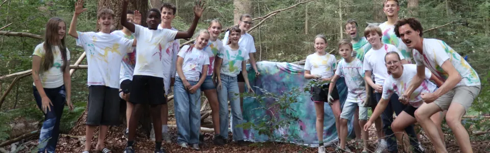 Tieners en leiding poseren vrolijk in kleurrijk beschilderde shirts in het bos.