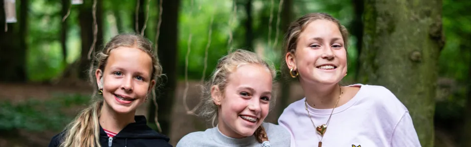 Drie lachende meiden poseren samen tijdens brugkamp in het bos