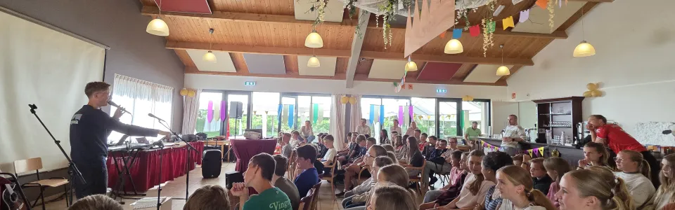 Tieners luisteren aandachtig naar livemuziek in de feestelijk versierde kampzaal.
