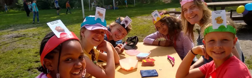Lachende kinderen spelen samen een raadspel aan de kamptafel