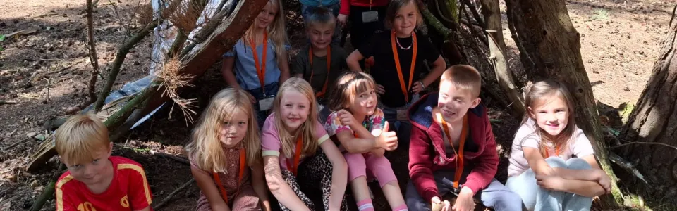Kinderen poseren trots bij hun zelfgebouwde boshut tijdens kamp.