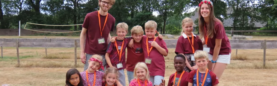 Kampleiders poseren lachend met hun groep kinderen op het veld