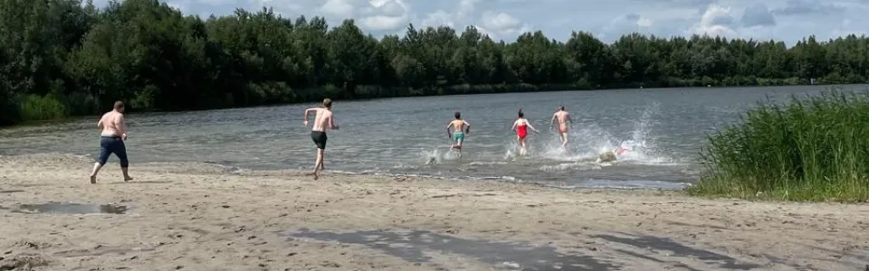 Tieners rennen enthousiast vanaf het strand het meer in
