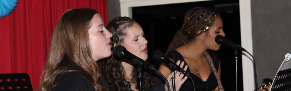 Drie meiden zingen samen, begeleid door een akoestische gitaar