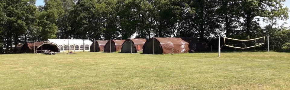 Groot grasveld met tenten en speelruimte op het terrein