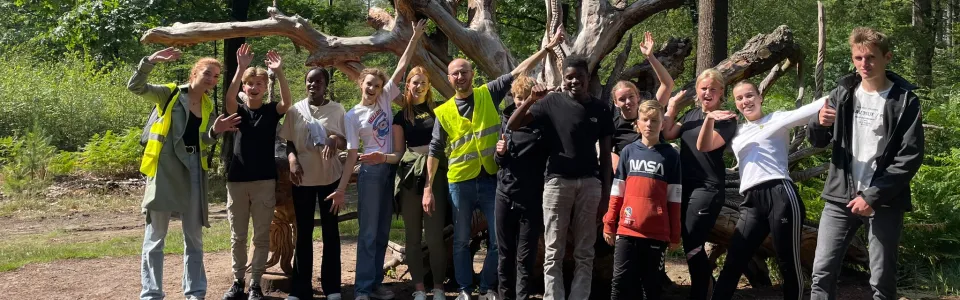 Groep deelnemers bij een grote boomstronk in het bos