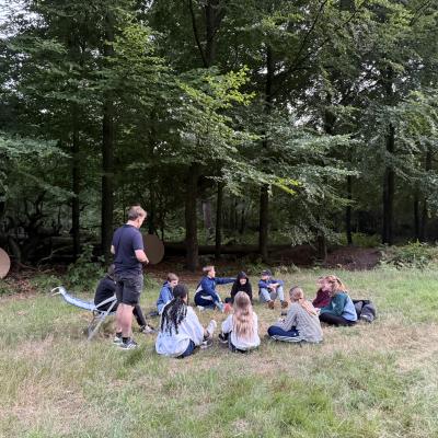 Deelnemers zitten in het gras bij de bosrand